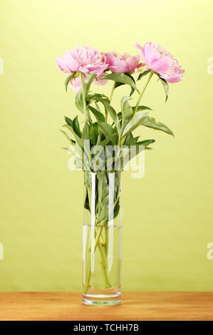Drei rosa Pfingstrosen in Vase auf Holztisch auf grünem Hintergrund Stockfoto
