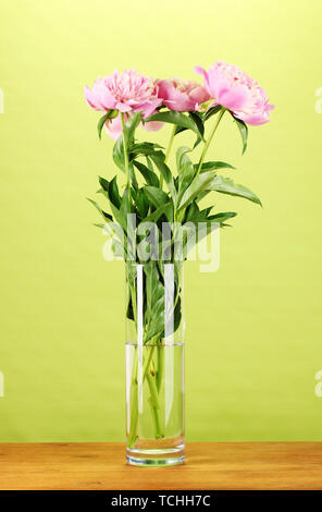 Drei rosa Pfingstrosen in Vase auf Holztisch auf grünem Hintergrund Stockfoto