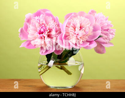 Drei rosa Pfingstrosen in Vase auf Holztisch auf grünem Hintergrund Stockfoto