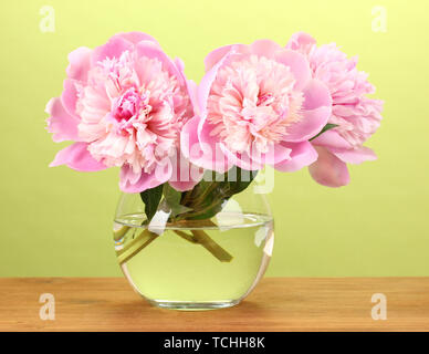 Drei rosa Pfingstrosen in Vase auf Holztisch auf grünem Hintergrund Stockfoto
