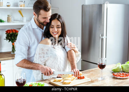 Glückliches Paar stehen gemeinsam in der Küche, während man schneiden Brot auf Schneidebrett Stockfoto