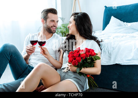 Paar mit klirren Gläser Rotwein und Frau mit Blumenstrauß aus roten Rosen Stockfoto