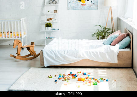 Holz Schaukelpferd in der Nähe von Bed mit weißer Bettwäsche und Spielzeug Bausteine auf dem Teppich Stockfoto