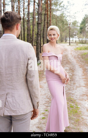 Lächelnde Mädchen in rosa Kleid bei Bräutigam im Wald suchen Stockfoto