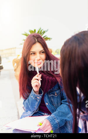 Zwei junge Frauen, von Afrikanischen und kaukasischen Ethnie, Studie im Freien auf einer Bank sitzen. Stockfoto