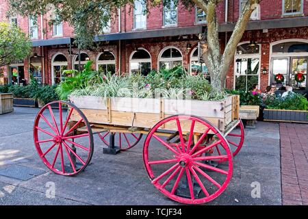 Ein wagon wheel Warenkorb mit Blumen gefüllt sitzt in der Spaziergang unter den historischen Gebäuden in Savannah, Georgia Stockfoto