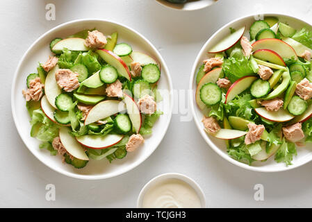 Gesunde Ernährung Essen. Thunfisch Salat mit Scheiben Gurke, Avocado, roter Apfel auf die Platte über der weißen Stein Hintergrund. Ansicht von oben, flach Stockfoto