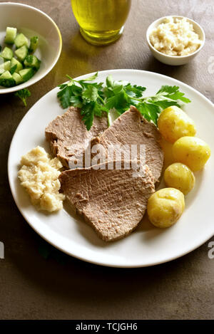 Tafelspitz, gekochtes Rindfleisch mit Kartoffeln und Meerrettich auf braunem Hintergrund. Stockfoto
