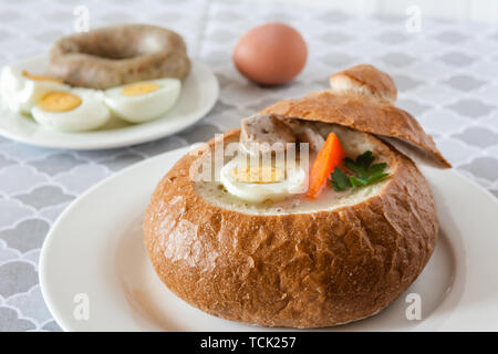 Die saure Suppe (zurek) von Roggenmehl mit Wurst und Ei in Brot Schüssel serviert. Traditionelle polnische saure Roggen Suppe, beliebt Ostern Gericht. Stockfoto