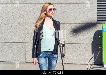 Schöne Frau mit Netzstecker in der Hand geht an das Auto zum Aufladen Stockfoto