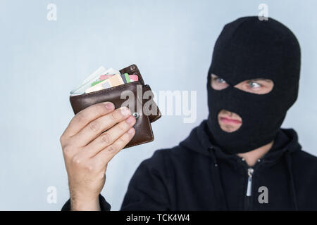 Dieb in schwarze Maske holding Wallet und Kamera. Der Räuber in der Balaclava zählt das Geld in der Brieftasche gestohlen. Stockfoto