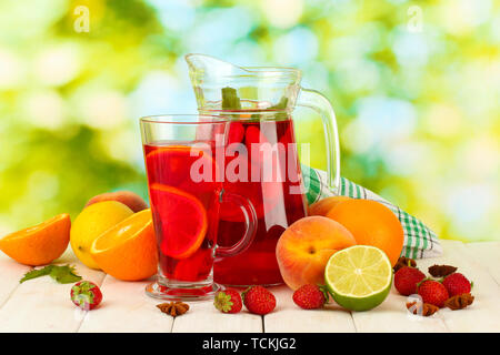 Sangria in Krug und Glas mit Früchten, auf Holztisch, auf grünem Hintergrund Stockfoto