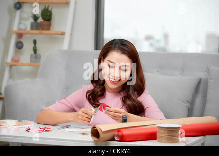 Lächelnde Mädchen schneiden valentine Herz aus rotem Papier mit einer Schere im Wohnzimmer Stockfoto