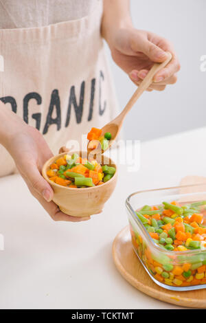 Schöpfkelle aus gedämpftem frisch geernteten jungen Gemüse, einschließlich Crinkle cut geschnittene Karotten, Erbsen und Kartoffeln für eine gesunde Begleitung zum Abendessen Stockfoto