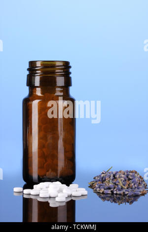 Flasche mit Pillen und Kräutern auf blauem Hintergrund Konzept der Homöopathie Stockfoto