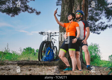 Glückliches Paar mit Mountainbike unter selfie Smartphone im Freien. Ein glückliches Paar, die einen aktiven Lebensstil, in den Wäldern in der Nähe des Baums zu Stillstand führen. Stockfoto