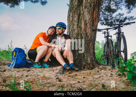 Glückliches Paar mit Mountainbike sitzen umfassende Freizeitaktivitäten Natur. glückliches Paar, führen einen aktiven Lebensstil, im Wald in der Nähe von Tree gestoppt eine Pause Stockfoto