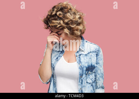 Portrait von traurig allein gedrückt junge Frau mit Curly Frisur im casual blaues Hemd stehen und mit dem Kopf nach unten und Weinen. indoor Studio shot, ich Stockfoto