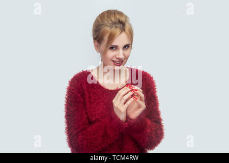 Portrait von lustig Schöne junge blonde Frau in Rot Bluse in gerissen betrügen Hände Geste und Kamera mit toothy Lächeln. Stockfoto