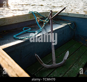 Ein großes metallisches Anker sitzt in einem kleinen blauen Ruderboot. Während einer frühen Sonnenuntergang auf einem kleinen See genommen Stockfoto