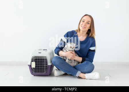 Charmante positive junge Frau hält in ihrer Hände ihre schönen grauen schottischen Katze sitzt auf dem Boden in eine neue Wohnung. Pet-Konzept. Stockfoto