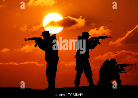 Silhouette der militärischen drei Soldaten oder Offizier mit Waffen bei Sonnenuntergang. schoß, Gewehr, bunte Himmel, Berge, Hintergrund, Team Stockfoto