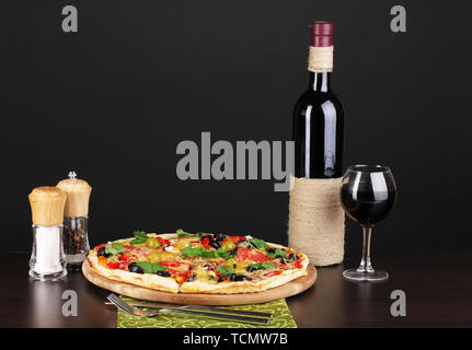 Leckere Pizza mit einem Glas Rotwein und Gewürzen auf Holztisch auf schwarzem Hintergrund Stockfoto