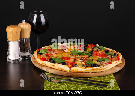 Leckere Pizza mit einem Glas Rotwein und Gewürzen auf Holztisch auf schwarzem Hintergrund Stockfoto