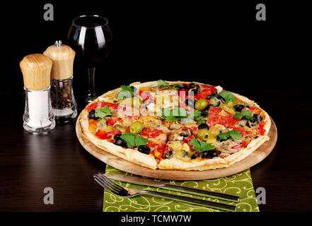 Leckere Pizza mit einem Glas Rotwein und Gewürzen auf Holztisch auf schwarzem Hintergrund Stockfoto