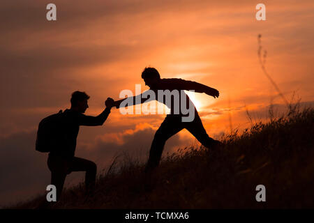 Teamarbeit von zwei Männern, die Wanderer, die sich gegenseitig helfen auf Bergsteigen Team, wunderschönen Sonnenuntergang Landschaft. Sport und aktiv leben Konzept Stockfoto