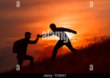 Teamarbeit von zwei Männern, die Wanderer, die sich gegenseitig helfen auf Bergsteigen Team, wunderschönen Sonnenuntergang Landschaft. Sport und aktiv leben Konzept Stockfoto