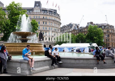 London, Großbritannien, Juni 9th 2019 Trafalgar Square, London, Großbritannien. Londoners und Touristen entspannen am Brunnen. Stockfoto