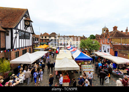 Le Wochenende Fall französischen Markt in Sandwich, England. Hohe Blickwinkel betrachten. Französische Marktstände in der Stadt mit vielen Menschen. Mittelalterlichen guildhall auf der linken und der mittelalterlichen Häuser im Hintergrund. Stockfoto