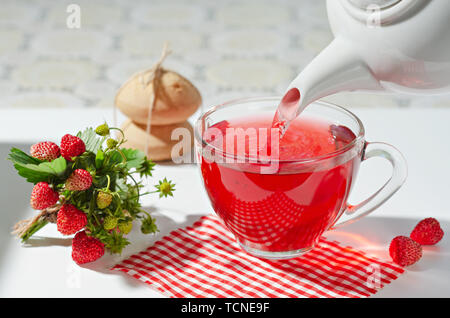 Heiße Tasse Berry Tee wird aus einer Teekanne in ein Glas Schale, Cookies und einem Bouquet von Beeren gegossen. Selektive konzentrieren. Stockfoto