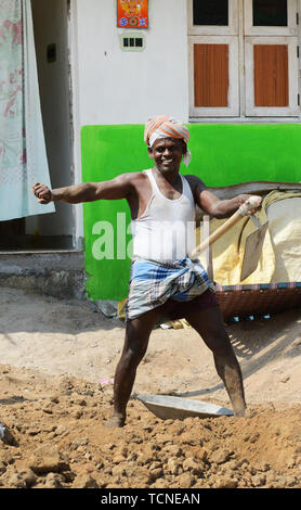 Ein tamilischer Mann Laden einer schweren Korb von Sand auf einer Frau Arbeiter Kopf. Stockfoto