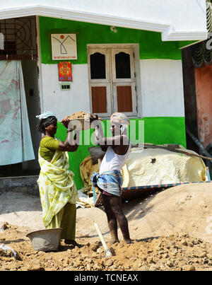 Ein tamilischer Mann Laden einer schweren Korb von Sand auf einer Frau Arbeiter Kopf. Stockfoto