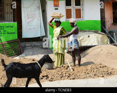 Ein tamilischer Mann Laden einer schweren Korb von Sand auf einer Frau Arbeiter Kopf. Stockfoto