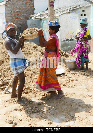 Ein tamilischer Mann Laden einer schweren Korb von Sand auf einer Frau Arbeiter Kopf. Stockfoto