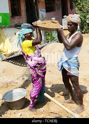 Ein tamilischer Mann Laden einer schweren Korb von Sand auf einer Frau Arbeiter Kopf. Stockfoto