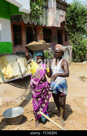 Ein tamilischer Mann Laden einer schweren Korb von Sand auf einer Frau Arbeiter Kopf. Stockfoto