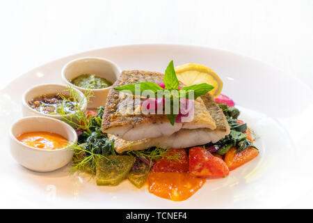 Nahaufnahme der gegrillten Pfanne gebratener Wolfsbarsch snapper Filet mit Gemüse- und italienischen Saucen, würzig, Mayo, Pesto, Oliven isoliert auf weiße Platte natürlichen b Stockfoto