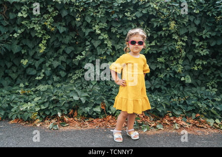 Portrait von Cute blonde Mädchen in der Kleidung posiert in sonniger Tag, und wenn man die Kamera im Freien Stockfoto