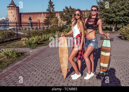 Zwei Mädchen Freundinnen Skateboard, im Sommer in der Stadt, Sie stehen, lange Haare Longboard für Skating. Mode ist der Lebensstil der Jugend Stockfoto