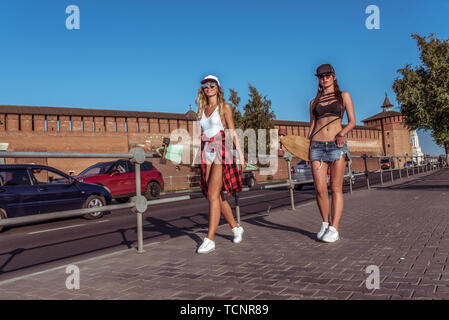 Zwei Mädchen Freundinnen Skateboard, Sommer Stadt, zu Fuß entlang der Straße, Hintergrund, langes Haar für longboarden. Mode ist der Lebensstil der Jugend Stockfoto