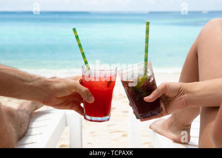 Die Paar Hände Toasten der Saft Gläser liegen auf Liegestuhl am Strand. Stockfoto