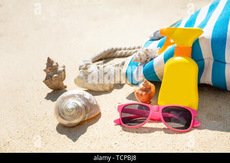 Sonnenbrille, Seashell, Sonnencreme und Handtasche am Strand