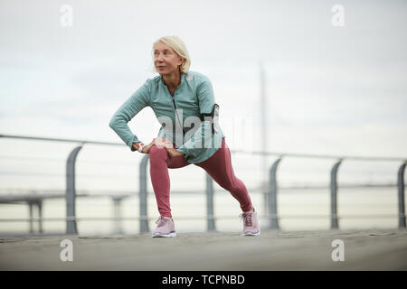 Reifen Sportlerin machen Übung für Beine stretching während der Arbeit aus auf der Brücke in der städtischen Umwelt auf Sommer Tag Stockfoto