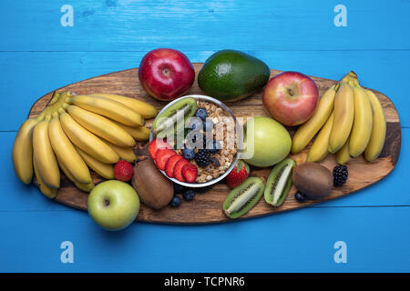 Blick von oben auf die hellen sortierte Früchte, Bananen, Äpfel, Mango, Kiwi, Erdbeeren, Blaubeeren, mit Getreide für ein gesundes Frühstück. Stockfoto