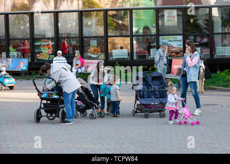 Nowosibirsk, Russland - 05.28.2019: Junge Mutter Mädchen mit Kinderwagen und Kleinkindern sind zu Fuß in einer Stadt Park vor dem hintergrund der grünen Bäumen, Stockfoto