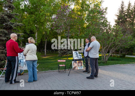 Nowosibirsk, Russland - 05.28.2019: Künstler mit Bildern von Leuten an der Staffelei in der Stadt Parks bieten ein Porträt auf einer warmen, klaren Tag Passanten zu zeichnen Stockfoto